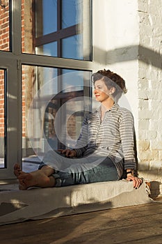 An active, beautiful middle-aged woman with a beautiful smile. Sitting on the windowsill near the window. Reflection in the window