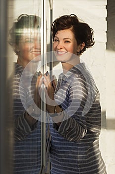 An active, beautiful middle-aged woman with a beautiful smile. Sitting on the windowsill near the window. Reflection in the window