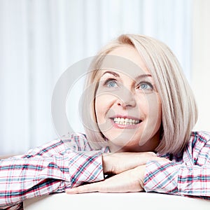 Active beautiful middle-aged woman smiling friendly and looking up at home in the living room. Woman's face close up