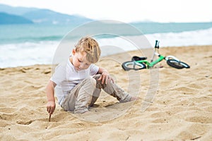 Active blond kid boy and bicycle near the sea. Toddler child dreaming and having fun on warm summer day. outdoors games for childr