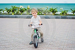 Active blond kid boy and bicycle near the sea. Toddler child dreaming and having fun on warm summer day. outdoors games for childr