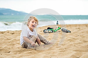 Active blond kid boy and bicycle near the sea. Toddler child dreaming and having fun on warm summer day. outdoors games for childr