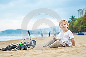 Active blond kid boy and bicycle near the sea. Toddler child dreaming and having fun on warm summer day. outdoors games for childr