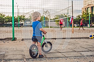 Active blond kid boy driving bicycle in the park near the sea. Toddler child dreaming and having fun on warm summer day. outdoors