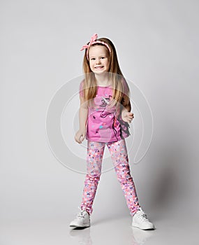 Active blonde kid girl in summer clothing colorful pants and t-shirt stands laughs and giggles