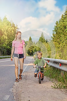 Active blonde mom walking with kid with bike. Family sport