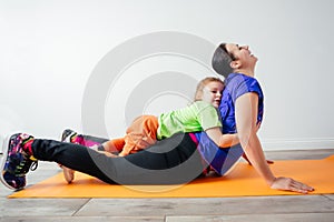 Active boy laying on his mother while she is standing in plank