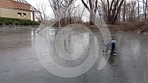 An active boy rolls on his knees on icy surface of lake. Happy child having fun outdoors in winter