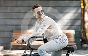 Active businessman riding a bicycle on way to job. Smiling guy in sunglasses and smartphone on bicycle