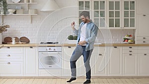 Active carefree young man enjoying funny dance standing in kitchen