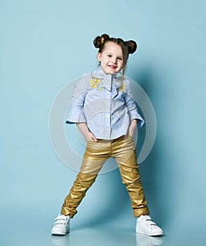 Active cheerful baby kid girl in blue shirt and gold leather pants is cool posing with her hands in her pockets, smiling