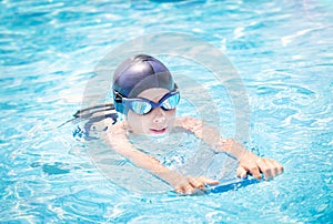 Active child (boy) doing water sport with swim board in the swimming pool. Healthy lifestyle.