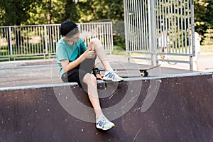 Active child boy after fall from skate board injured, sitting and looking at bruise on sport ramp on skate park