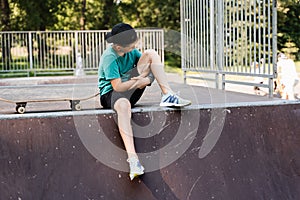 Active child boy after fall from skate board injured, sitting and looking at bruise on sport ramp on skate park