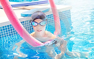 Active child (boy) ready to learns professional swimming with swim noodles and pool board in swimming pool.