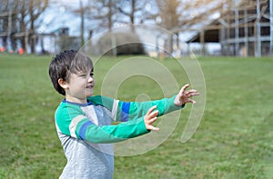 Active child looking out with hand rising up,Side view Portrait Happy young boy standing in the park with blurry grass fields and