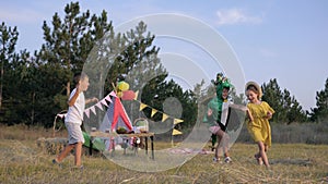 Active children, joyful little girl in carnival costume runs with her friends playing an energetic game in meadow in