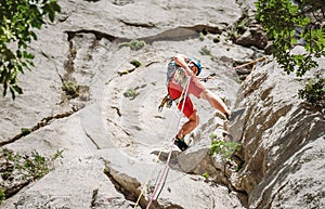 Active climber middle age man in protective helmet while abseiling from cliff rock wall using ropes with a belay device and photo