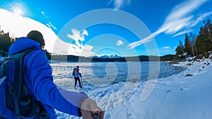 Active couple with hiking backpack watching the frozen lake Forstsee, Techelsberg, Carinthia (Kaernten), Austria, Europe