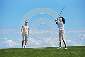 Active couple playing golf against blue sky with woman swinging golf club