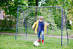 Active cute little kid boy playing soccer and football and having fun, outdoors. Child having game on rainy day. Wearing