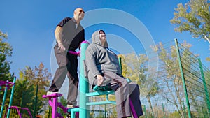 Active elderly couple doing sports on the simulator outdoors. Exercising outdoors in a park or garden in a health and