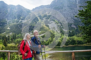 Active elderly couple hiking together in autumn mountains, on senior-friendly trail. Walking by lake, enjoying nature