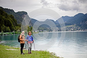 Active elderly couple hiking together in spring mountains. Senior tourists embracing each other in front of lake.