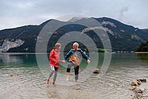 Active elderly couple hiking together in spring mountains, walking in cold water in mountain lake. Senior tourists