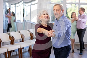 Active elderly couple in their free time is engaged in latin dance class and learns movements of cha-cha-cha dance