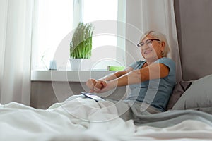 Active elderly female stretching her arms after sleeping