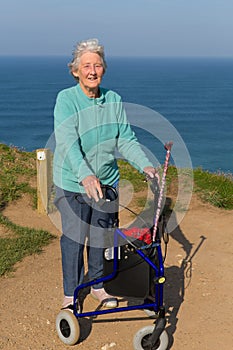 Active elderly lady pensioner in eighties with three wheel mobility frame by coast