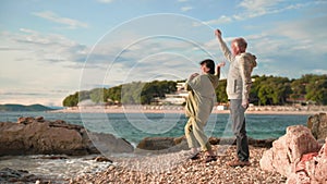 active elderly man and woman having fun throwing pebbles into sea during vacation for pensioners on a warm sunny evening