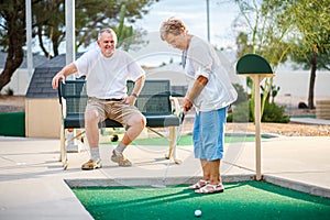 Active elderly senior couple playing miniature golf together