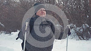 Active an elderly woman engaged in Nordic walking with sticks in the winter forest. Healthy lifestyle concept. Mature