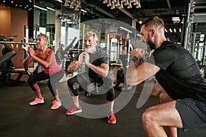 Active elderly woman and man performing squats in gym