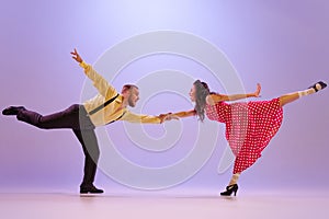Active and emotional couple in colorful retro style costumes dancing incendiary dances isolated on purple background in