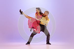 Active and emotional couple in colorful retro style costumes dancing incendiary dances  on purple background in