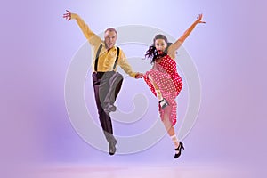 Active and emotional couple in colorful retro style costumes dancing incendiary dances  on purple background in