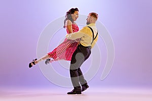 Active and emotional couple in colorful retro style costumes dancing incendiary dances  on purple background in