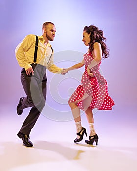 Active and emotional couple in colorful retro style costumes dancing incendiary dances  on purple background in