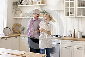 Active, energetic mature couple dancing in kitchen while cooking pastries