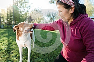 Active ethnic latin senior woman enjoying the outdoors with her pet dog, playing and petting him in the park