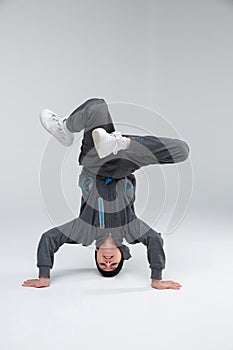 The active little boy, dances standing on head and arms, bending knees. On a gray background.