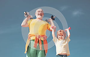 Active family enjoy sport and fitness. Funny old senior man and kid boy with dumbbells. Grandfather and child do morning