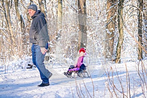 Active family holidays for adults and children. A man rides a little girl on a sled in the winter forest. Grandfather takes his