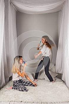 An active family young mother sings in a comb with a little daughter of school age. The older younger sister listens to a happy