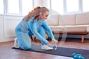 active fat woman sit on mat tying shoes laces on gumshoes ready practice fitness exercise