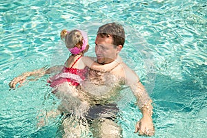 Active father teaching his child girl to swim in pool .