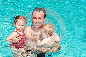 Active father teaching his children to swim in pool on tropical resort.